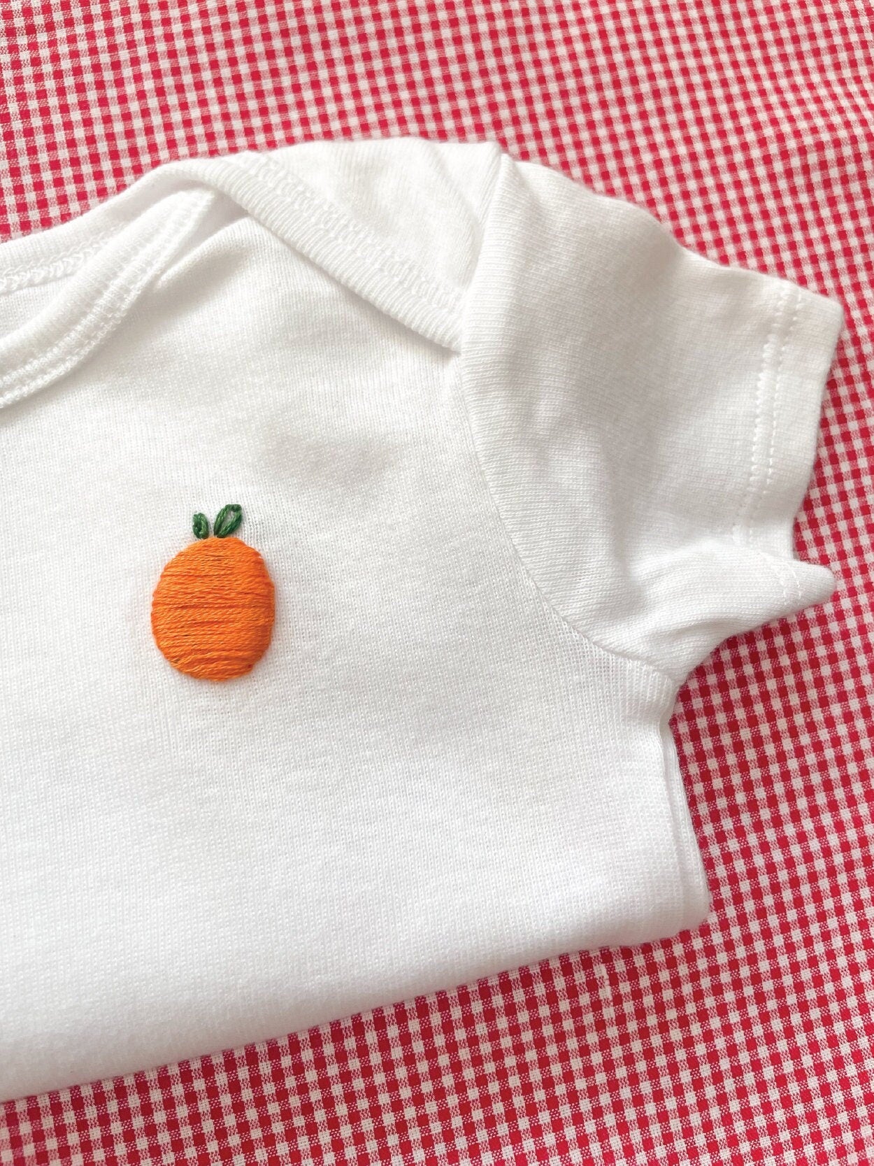 Orange hand embroidery on white baby onesie