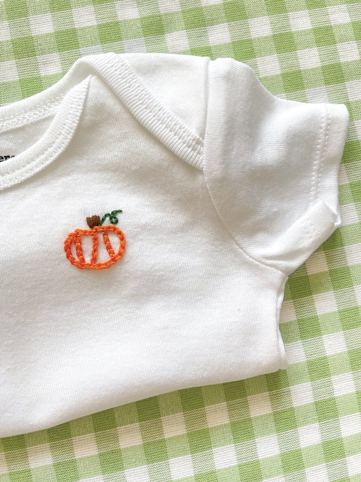 Detail image of hand-embroidered baby onesie featuring pumpkin motif on left chest