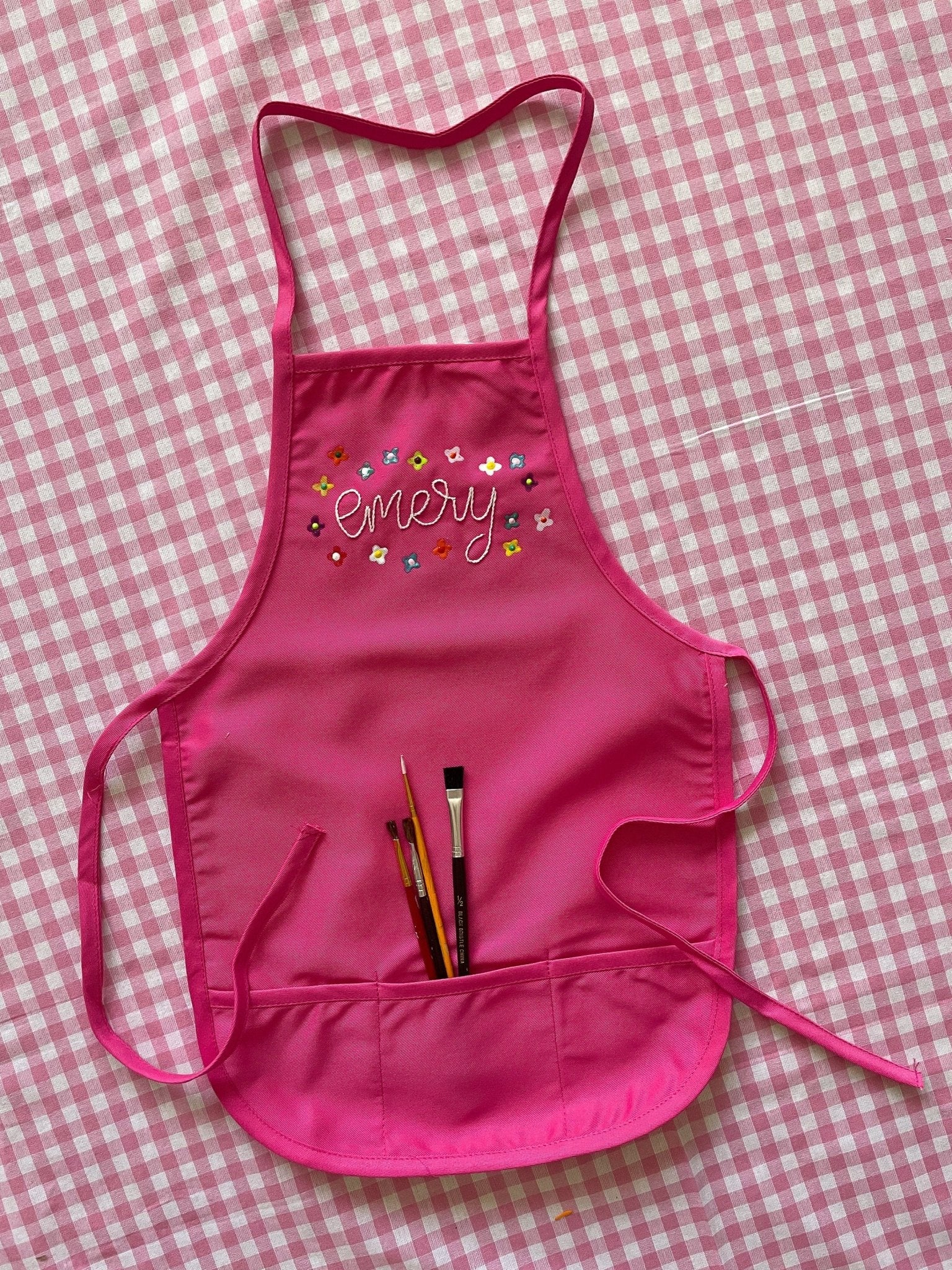 Hot pink children's apron embroidered with painted flowers around the name