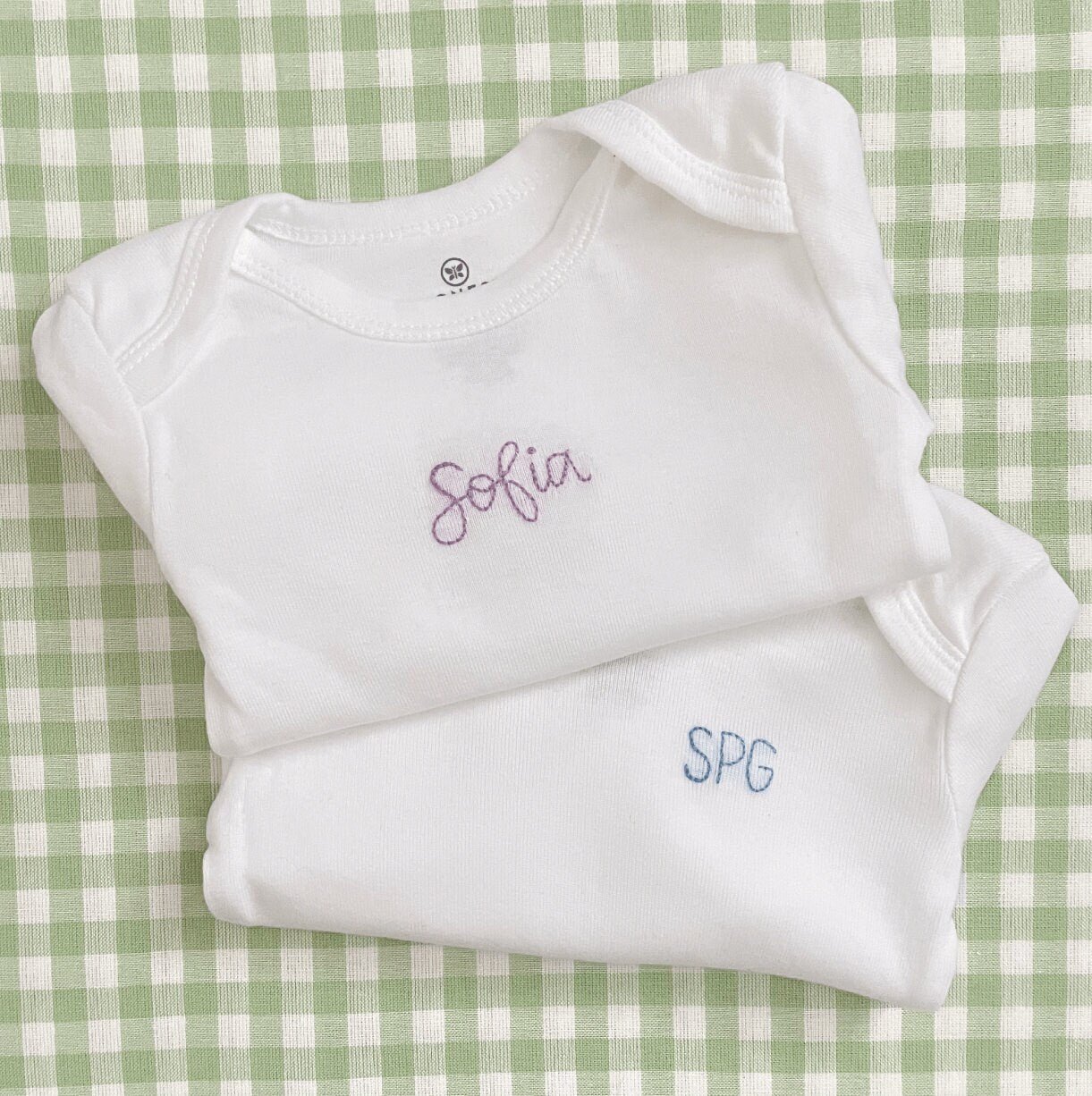 Set of hand embroidered baby bodysuits stacked on top of each other
