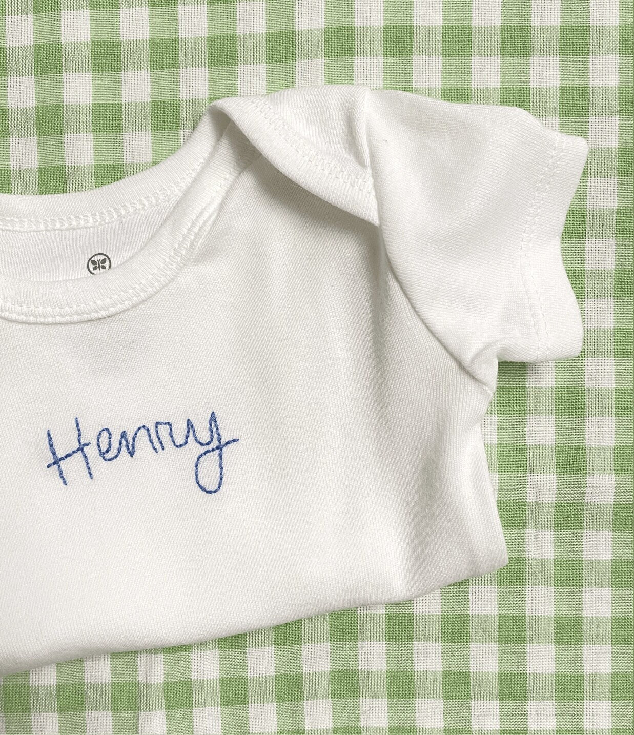 Folded hand embroidered baby bodysuit on a green and white checkered background