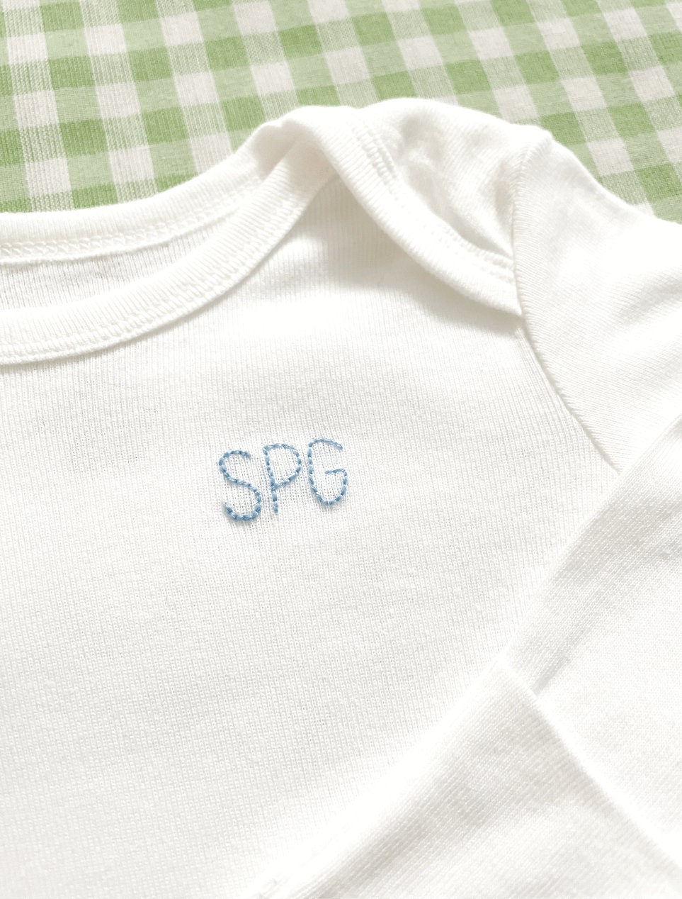 Baby's initials hand embroidered on left corner of white bodysuit