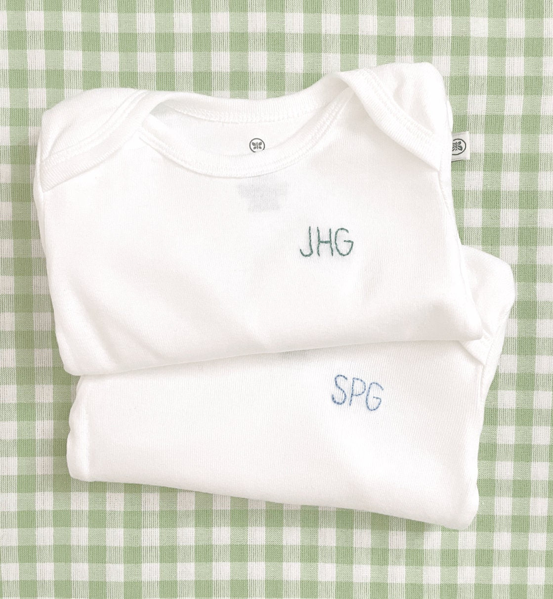 Set of hand embroidered baby bodysuits stacked on top of each other with 3 initials on left chest