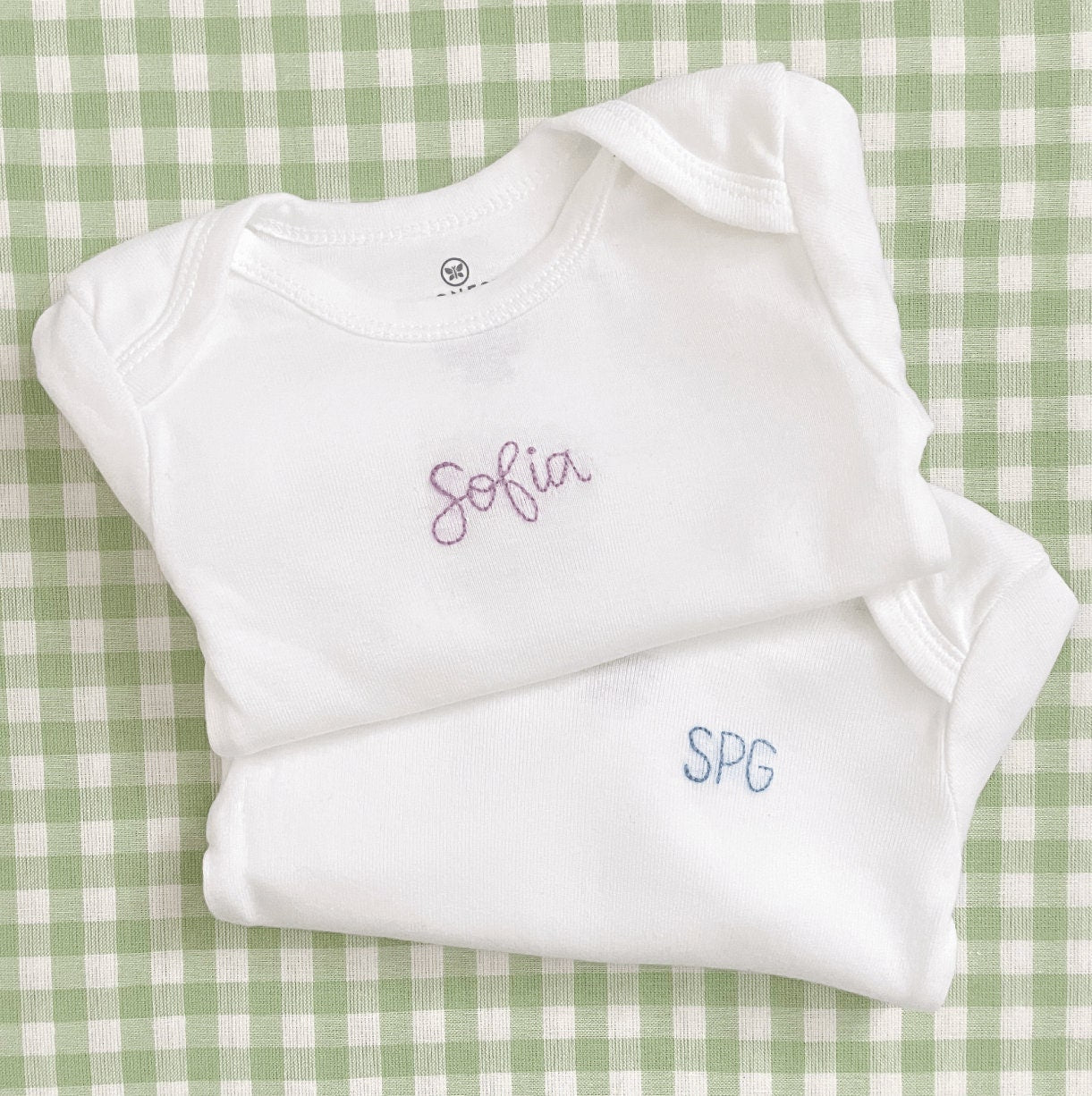 Set of hand embroidered baby bodysuits stacked on top of each other