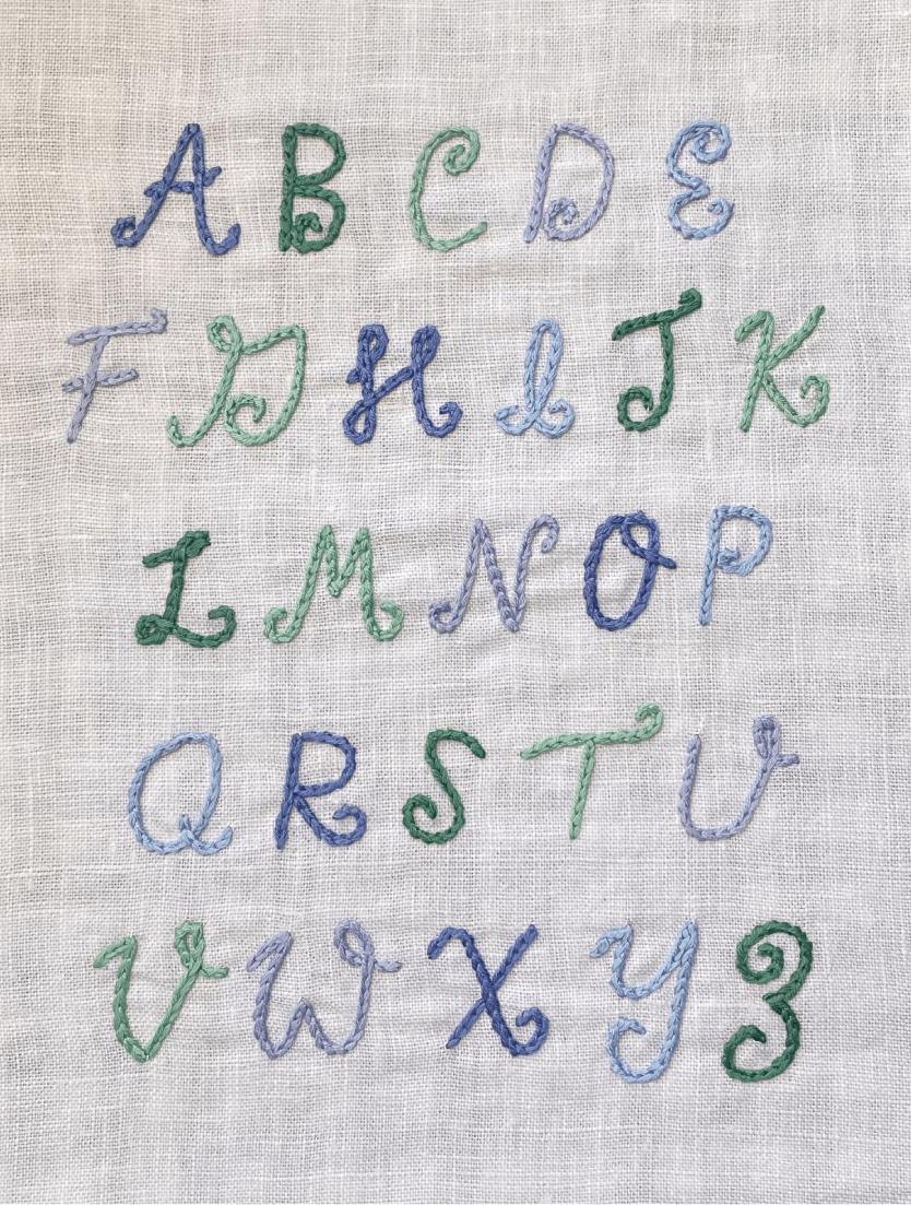 Hand embroidered alphabet in blue and green threads on a white linen background
