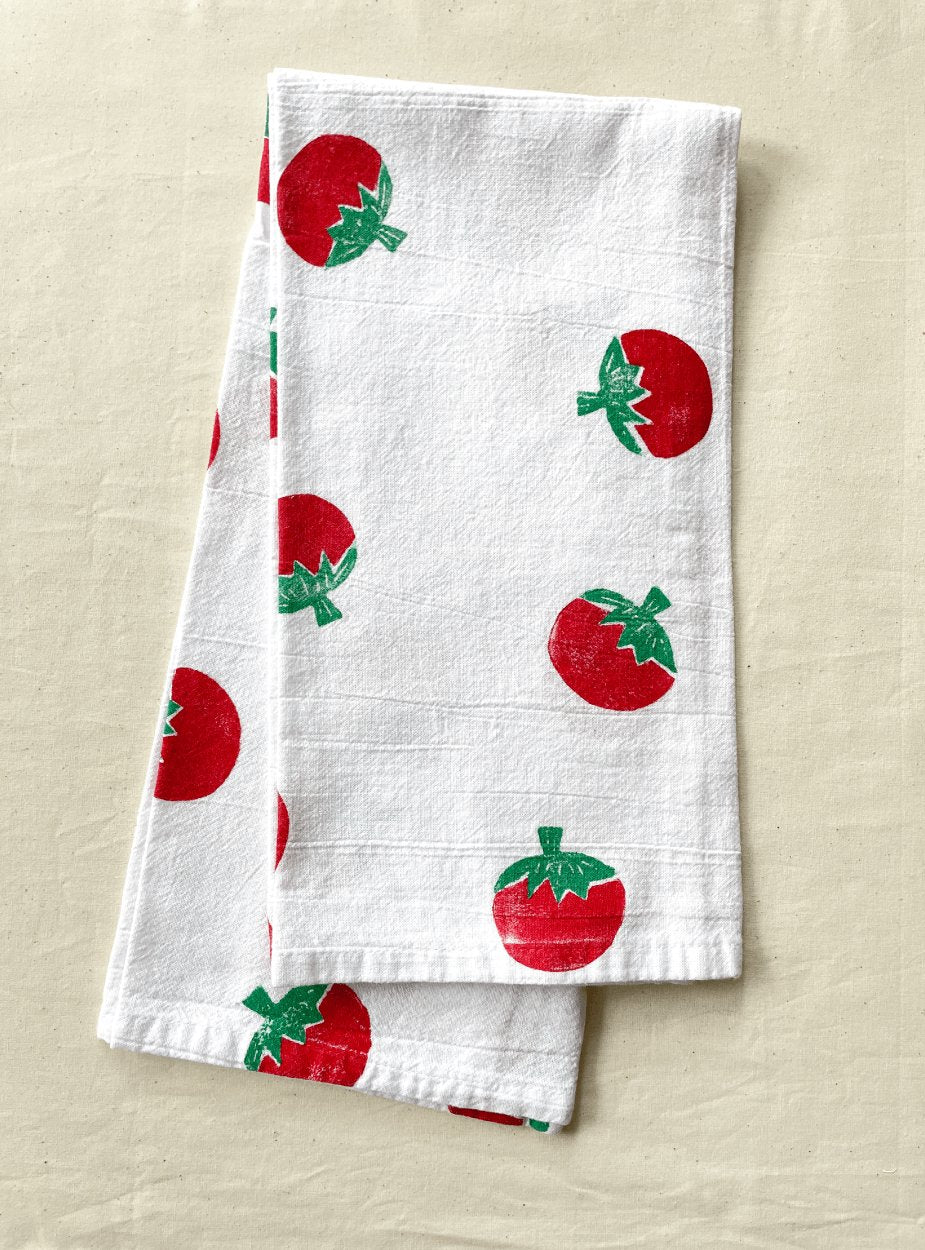 A white cotton tea towel with a red tomato block print pattern