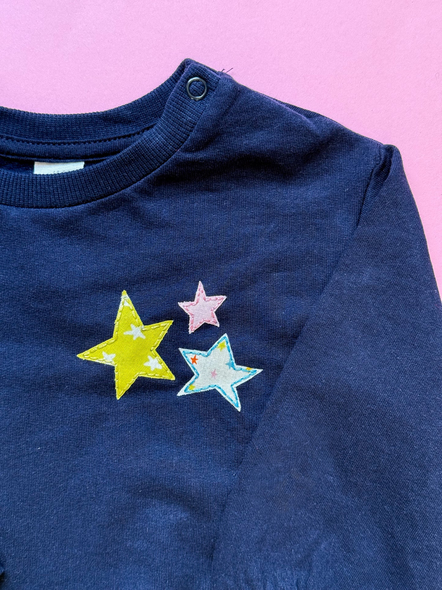 Kid's navy blue sweatshirt with colorful star designs hand embroidered and appliqued on a pink background