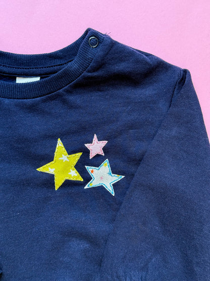 Kid's navy blue sweatshirt with colorful star designs hand embroidered and appliqued on a pink background