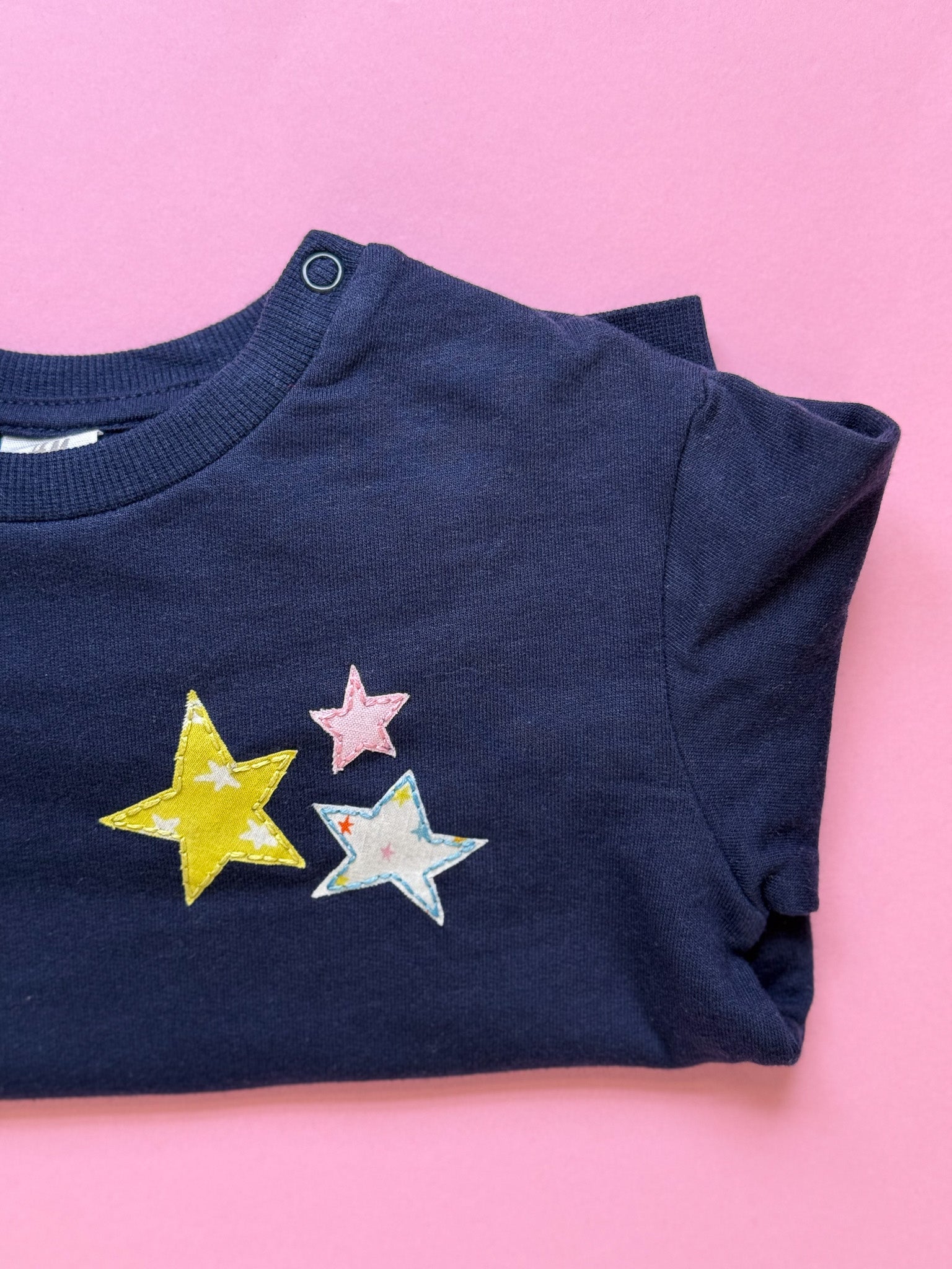 Navy blue child's sweatshirt with colorful star appliqués and hand embroidered stitching on a pink background