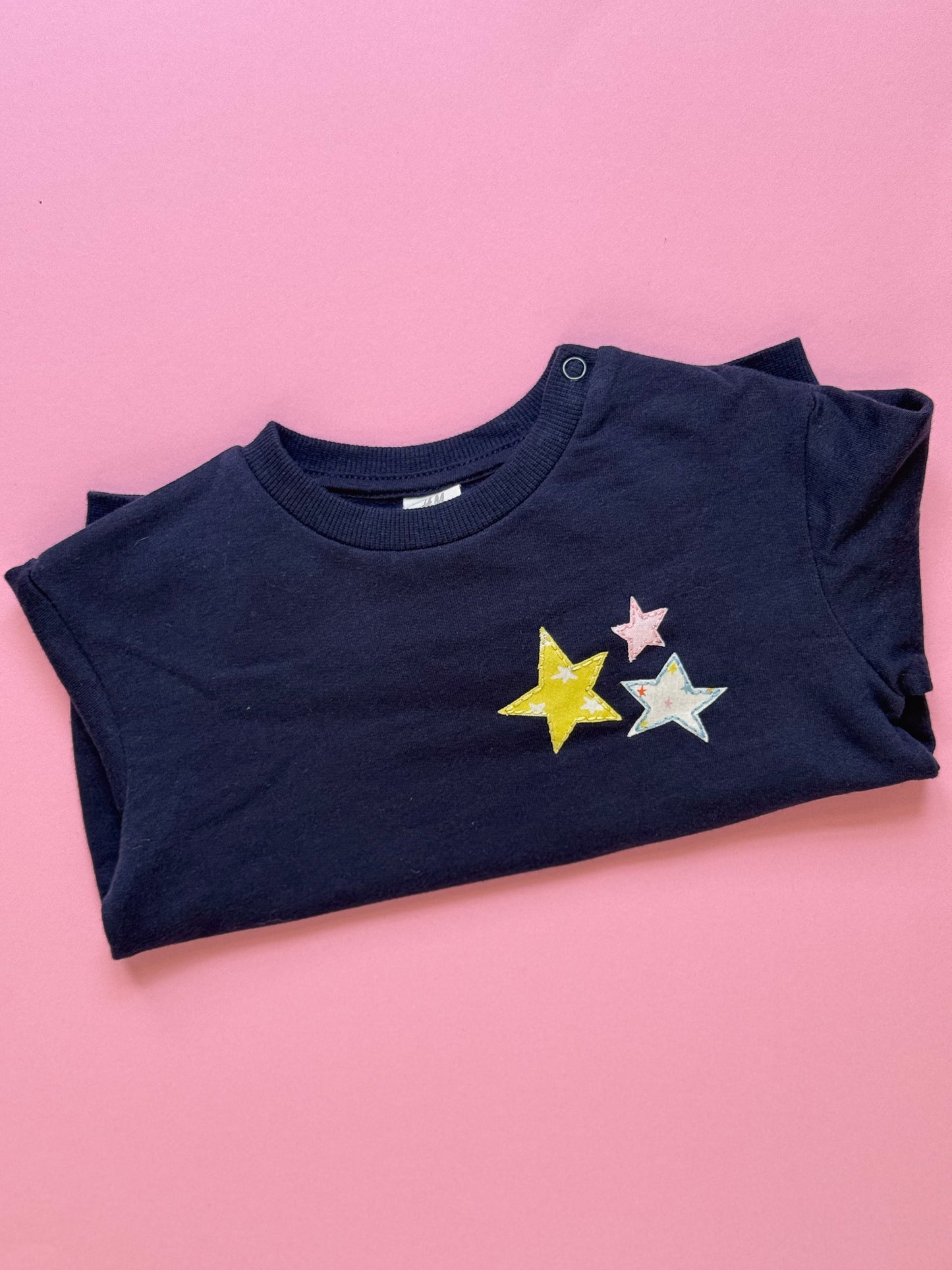 Folded navy blue sweatshirt with colorful star designs on a pink background