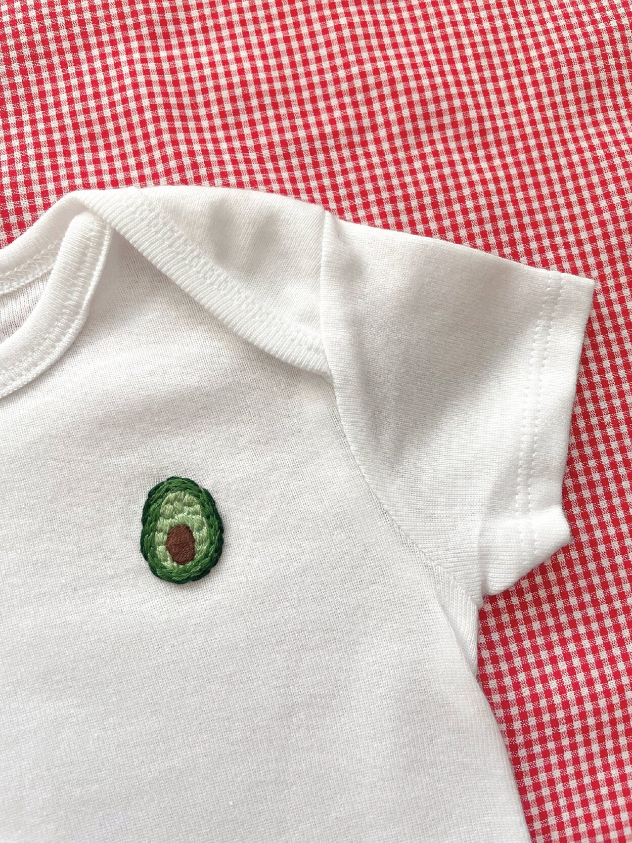 Avocado hand embroidery on white baby onesie