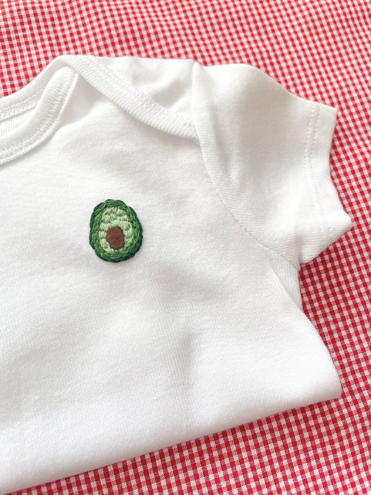 Avocado hand embroidery on white baby onesie