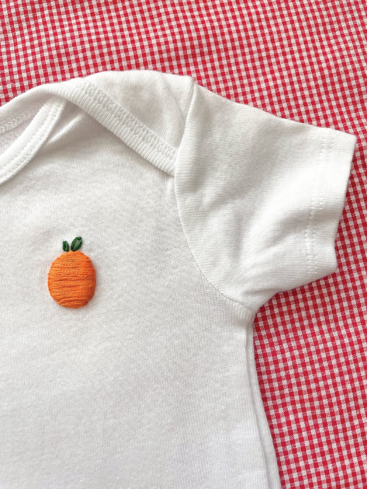 Orange hand embroidery on white baby onesie