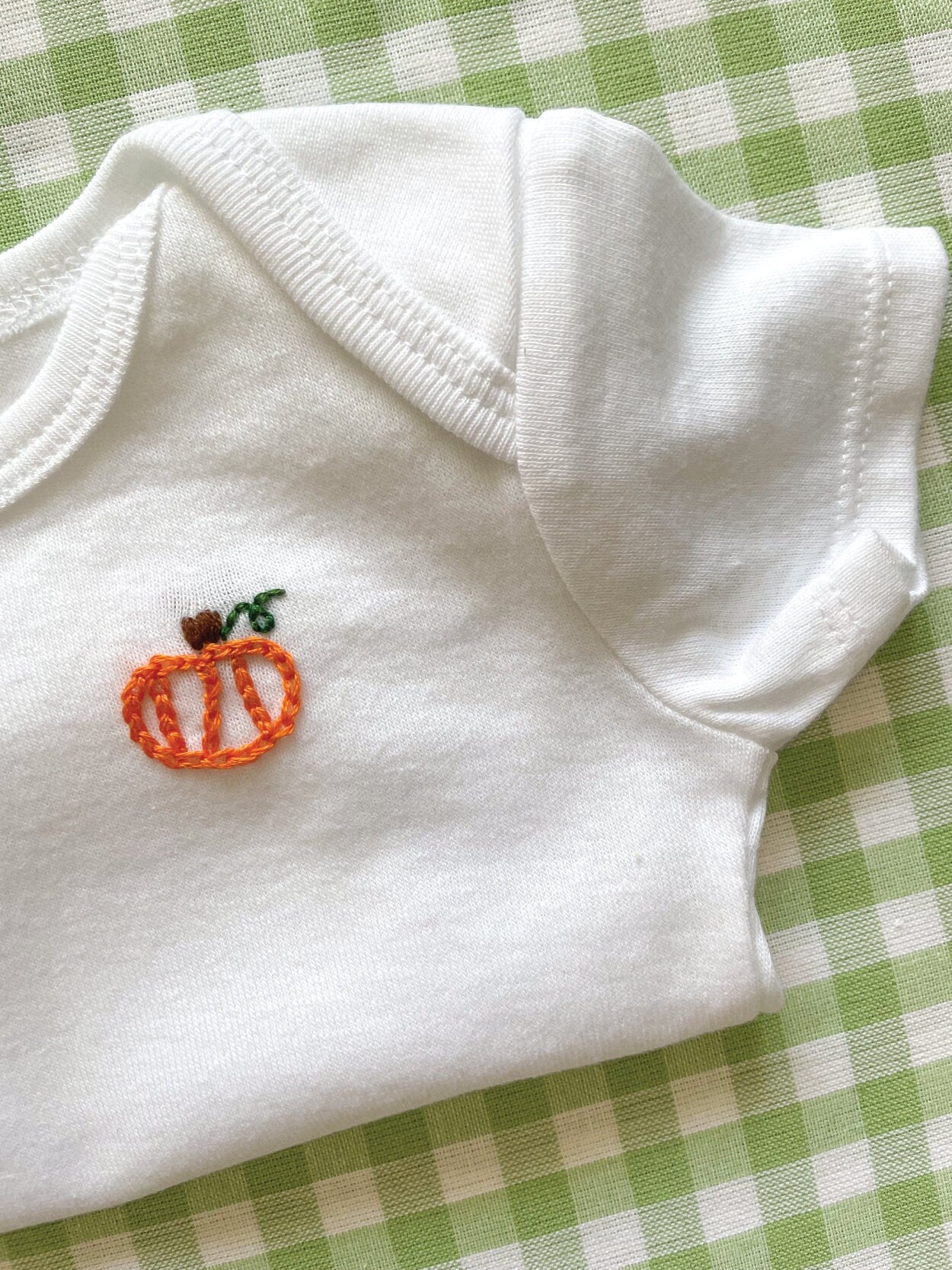 Detailed image of hand-embroidered baby onesie featuring pumpkin motif on left chest