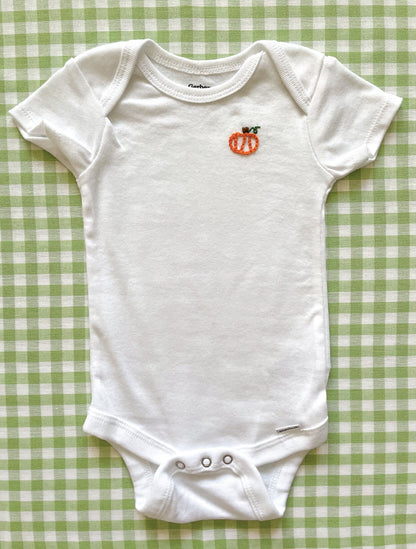 Full body image of hand-embroidered baby onesie featuring pumpkin motif on left chest