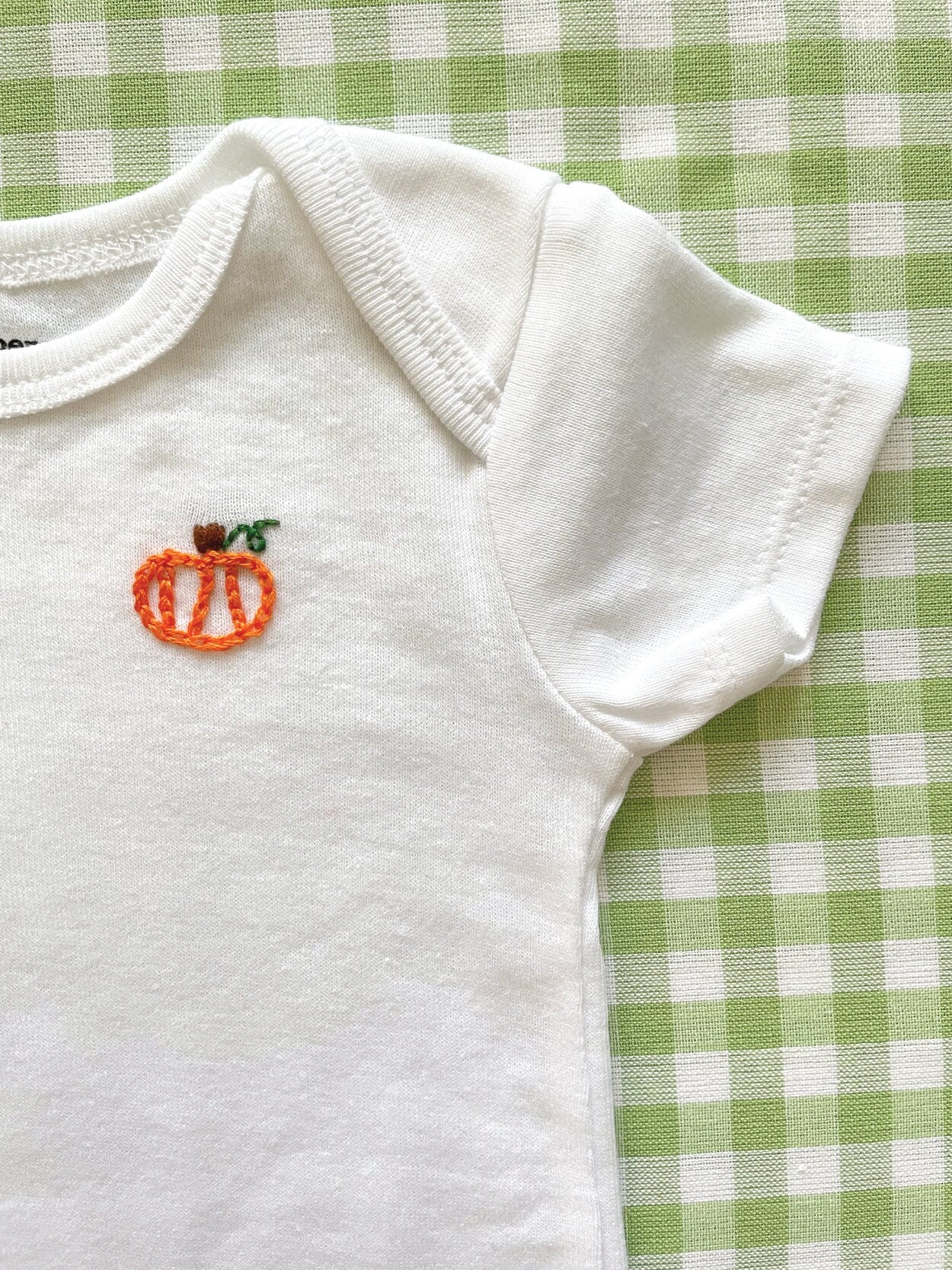 Up close image of hand-embroidered baby onesie featuring pumpkin motif on left chest