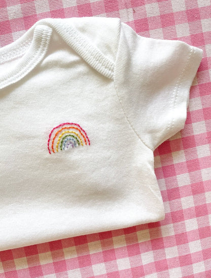 Detailed image of hand embroidered onesie featuring rainbow design in bright colors on left chest