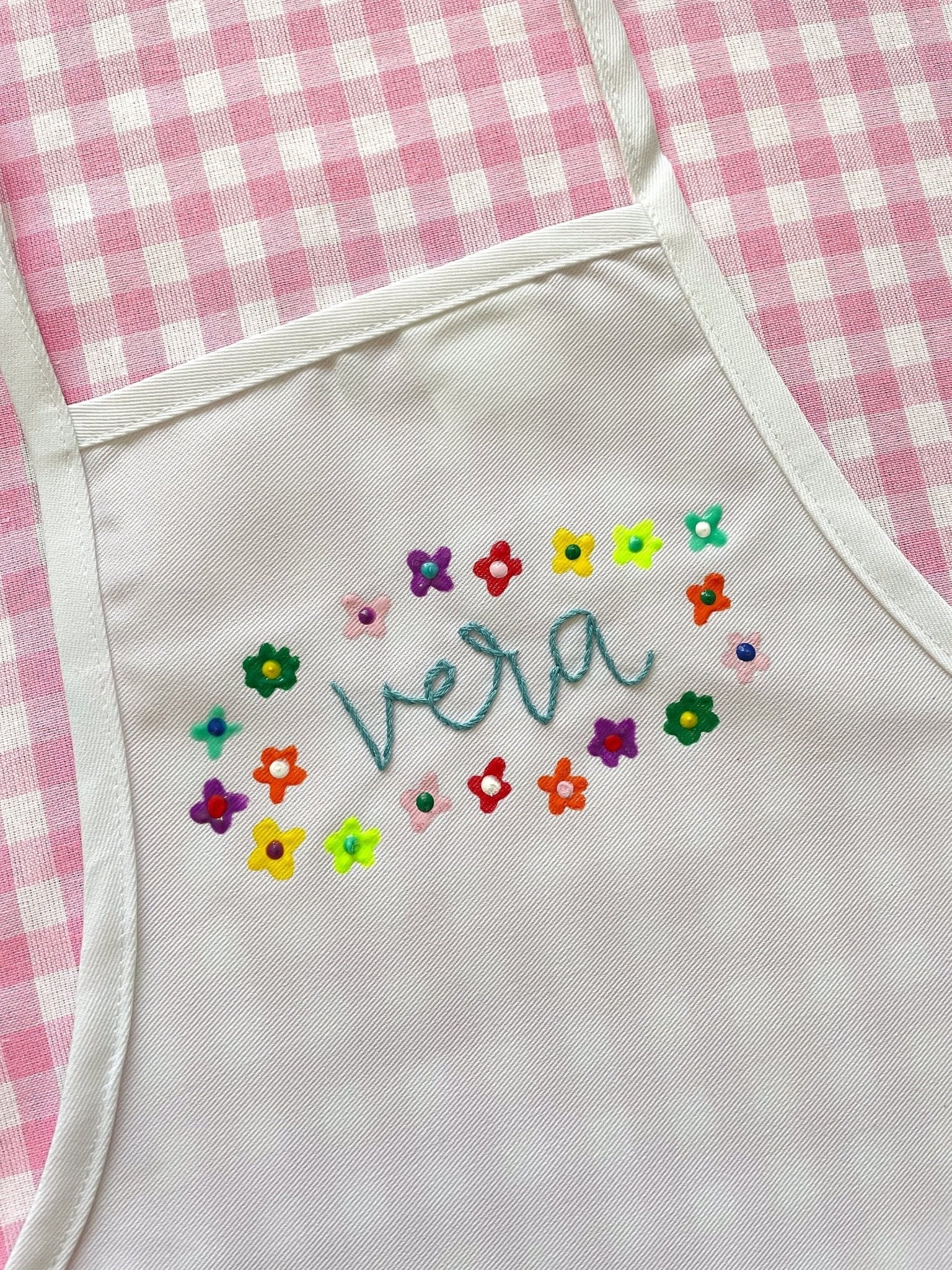 Top half of kid&#39;s apron embroidered with painted flowers around the name