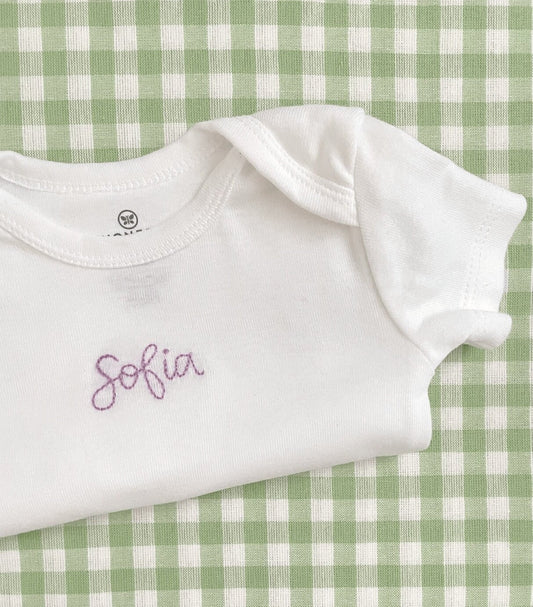 Folded hand embroidered baby bodysuit on a green and white checkered background